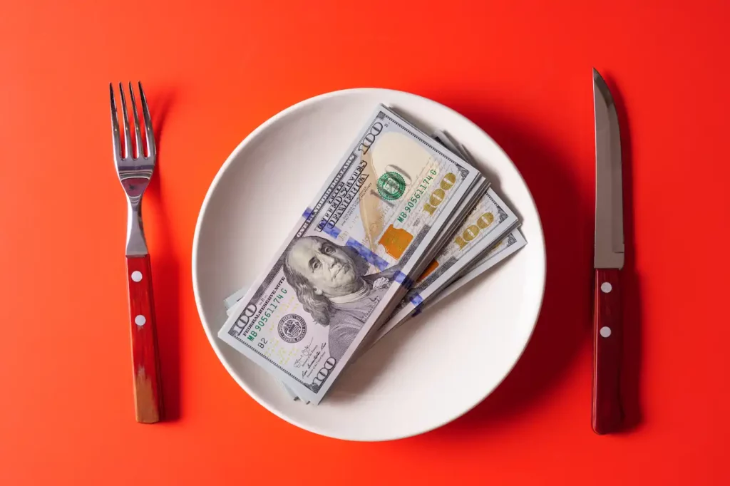 100 dollar bills on white plate on red background with knife and fork